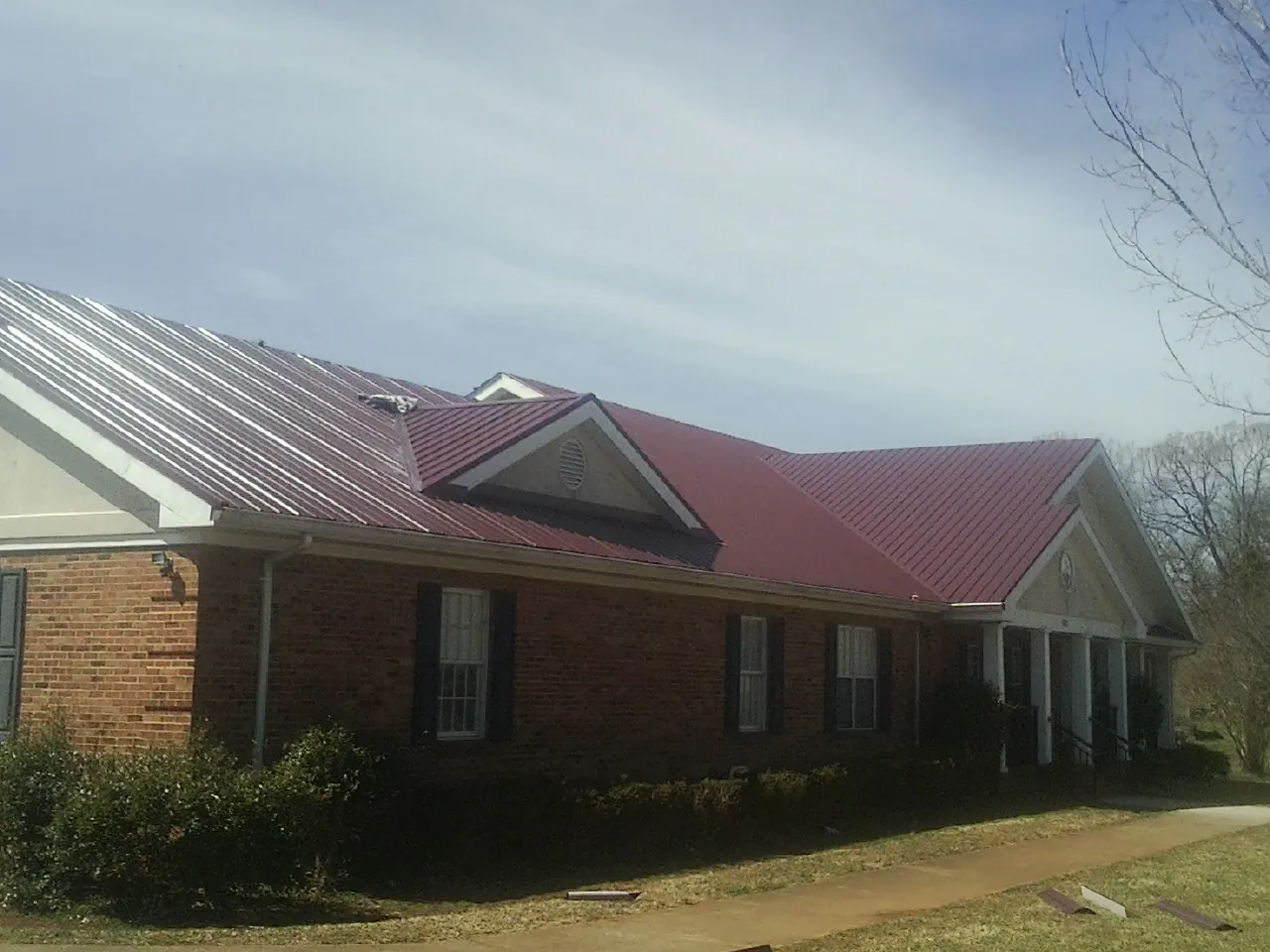 Red metal roof with gabled entries on a long brick building, from a Hail Damage Roof Repair job in Ursa