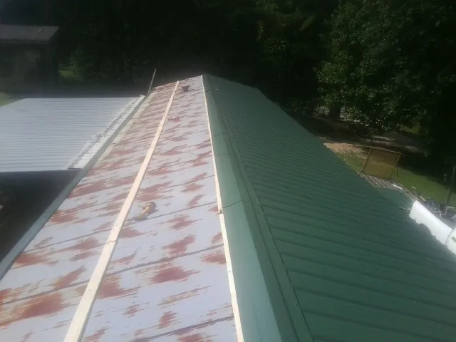 Old rusted panels beside newly installed green metal roofing — Wind Damage Roof Repair by Roofing Brothers in Ursa