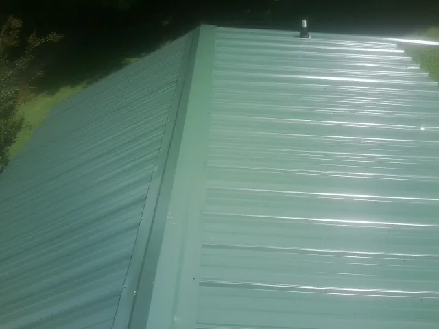 New green metal panels meeting at the ridge of a roof — Flat Roof Repair work by our crew in Ursa