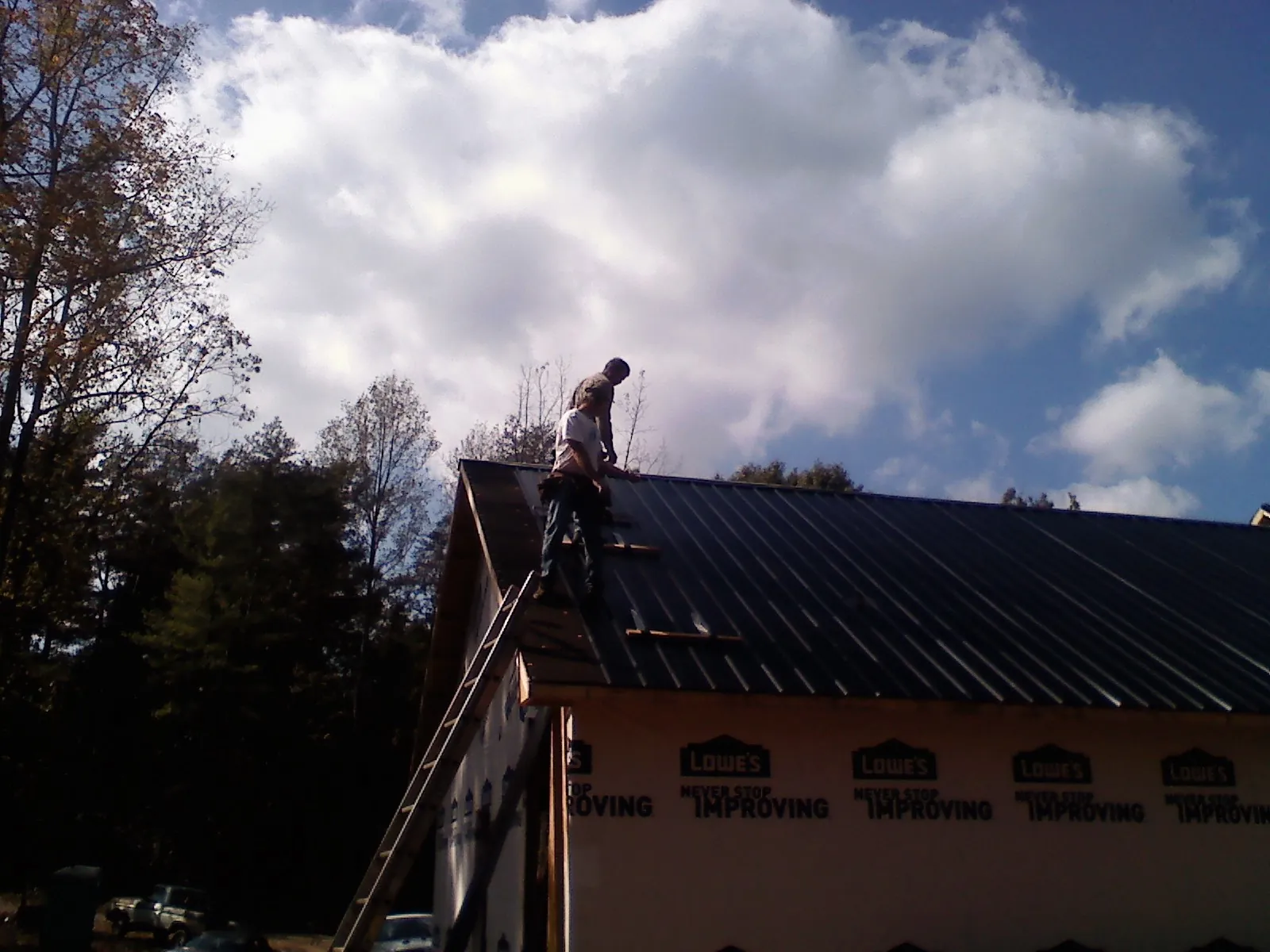 Roofer fastening dark metal panels high against a cloudy sky, from a Roof Inspection job in Ursa