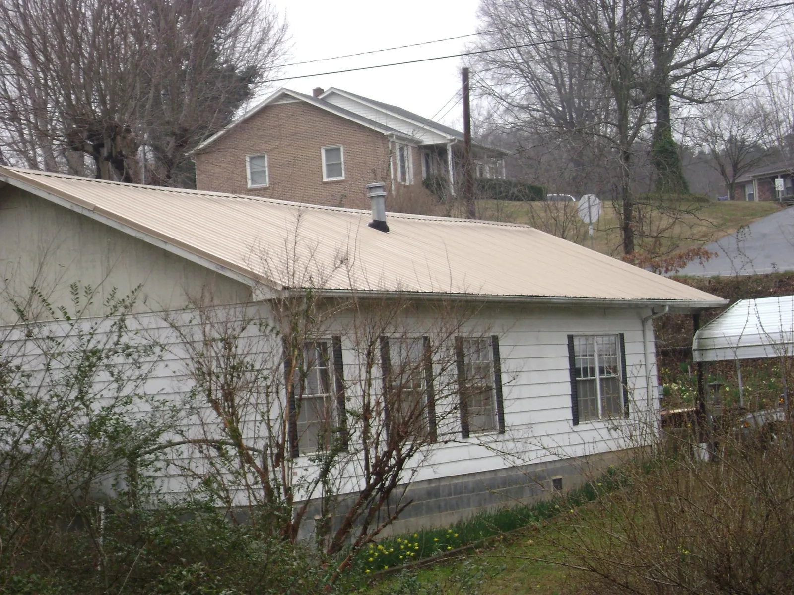 Tan metal roof on a white sided house set into a hillside — Commercial Roofing by Roofing Brothers in Ursa