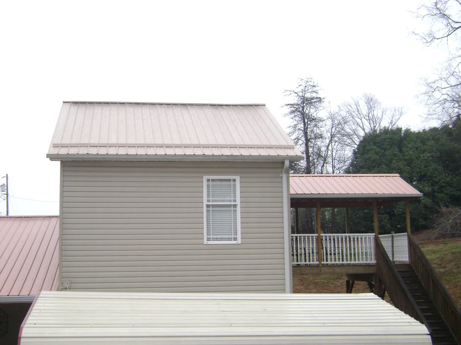 Tan metal roofs on a two story addition and attached porch, from a Roof Replacement job in Ursa